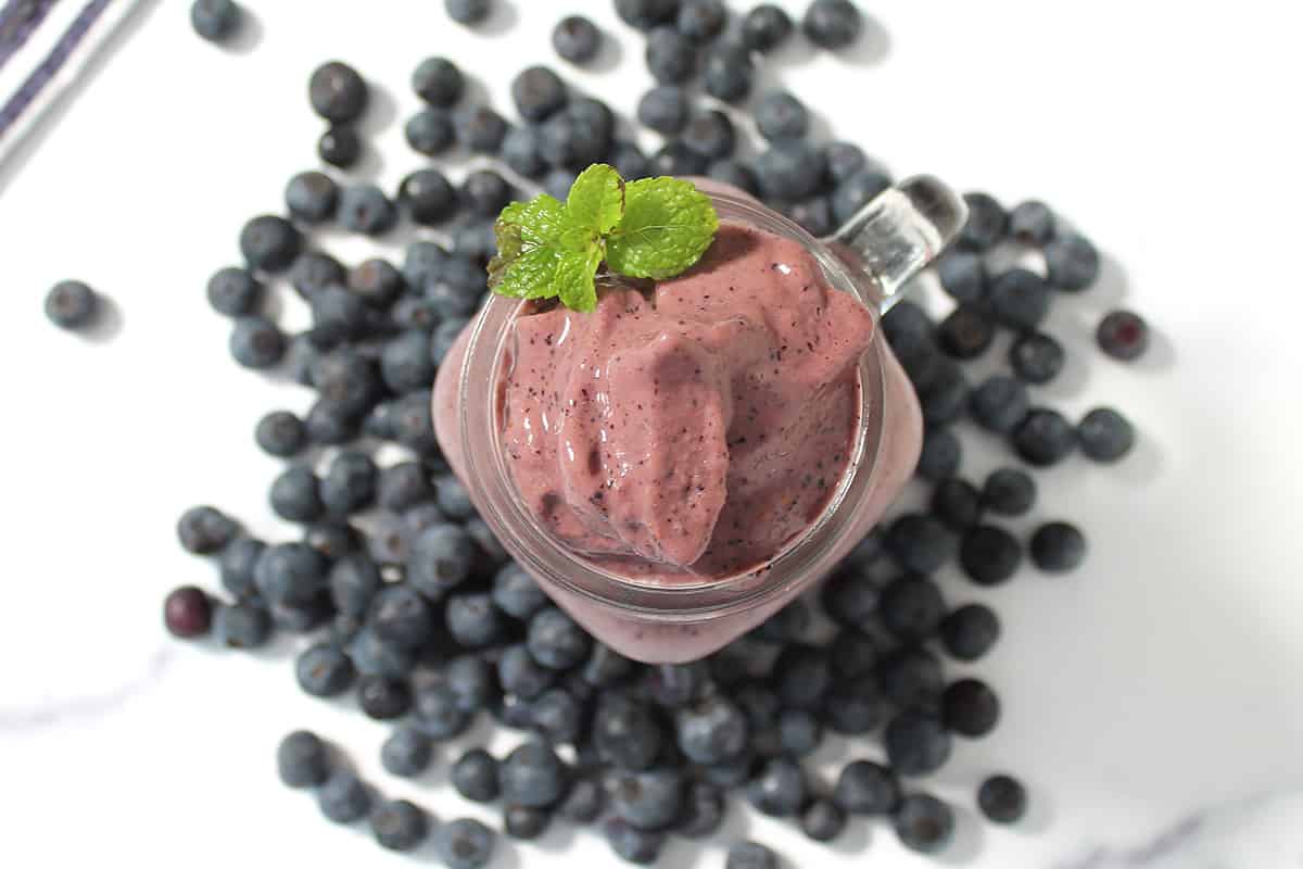 Overhead of blueberry protein smoothie amid blueberries on white table.