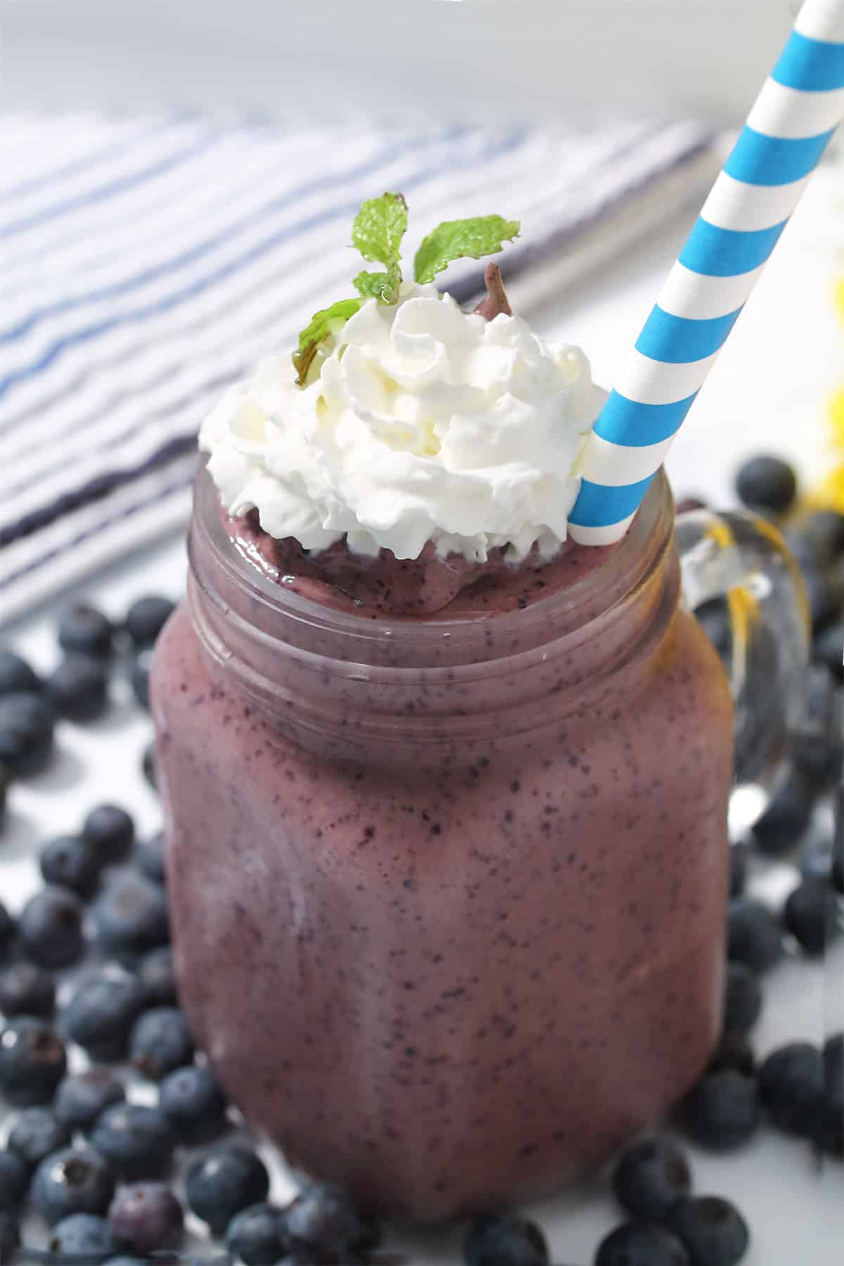 Protein smoothie in mason jar with whipped cream topping and striped straw.