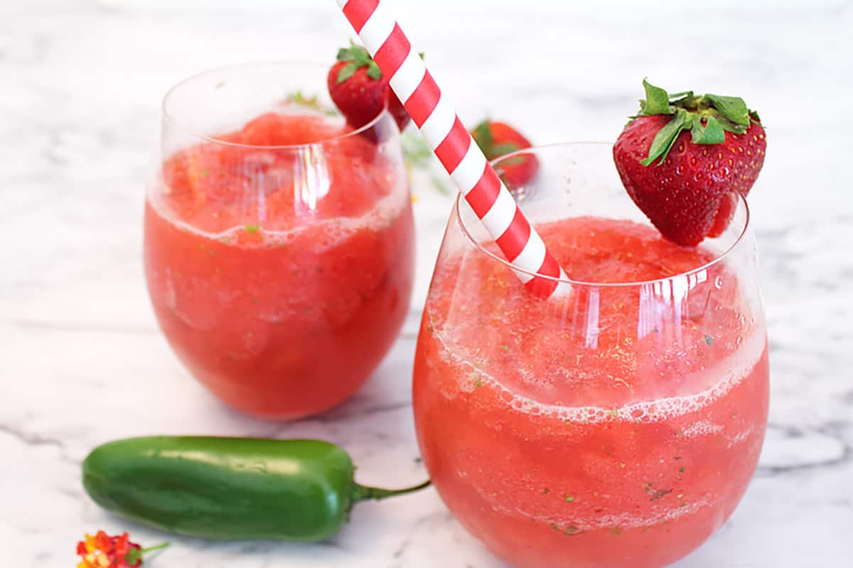 2 strawberry mules with strawberry garnish and straw on white table.