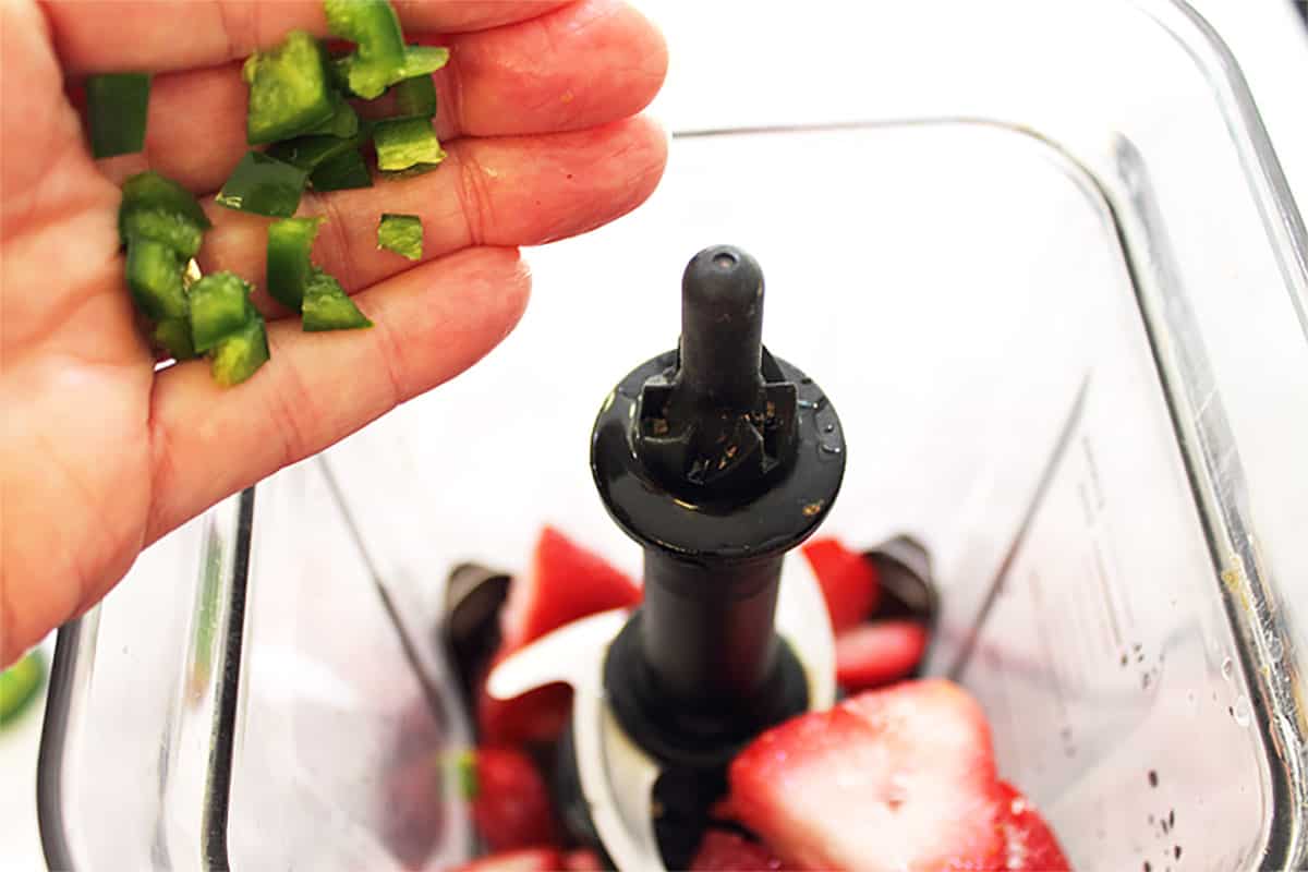 Adding jalapeno to strawberries in blender.