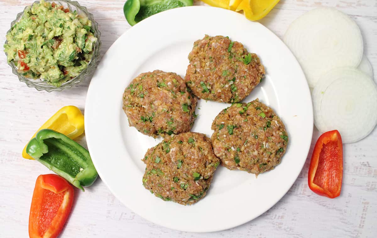 Prepared burgers on white plate surrounded by ingredients.