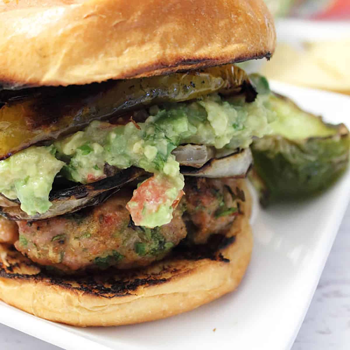 Closeup showing grilled burger with a heaping serving of guacamole on top.
