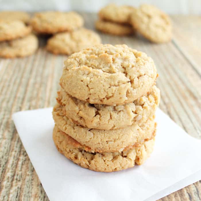 Stacked gluten free peanut butter cookies on parchment paper set on wooden table.