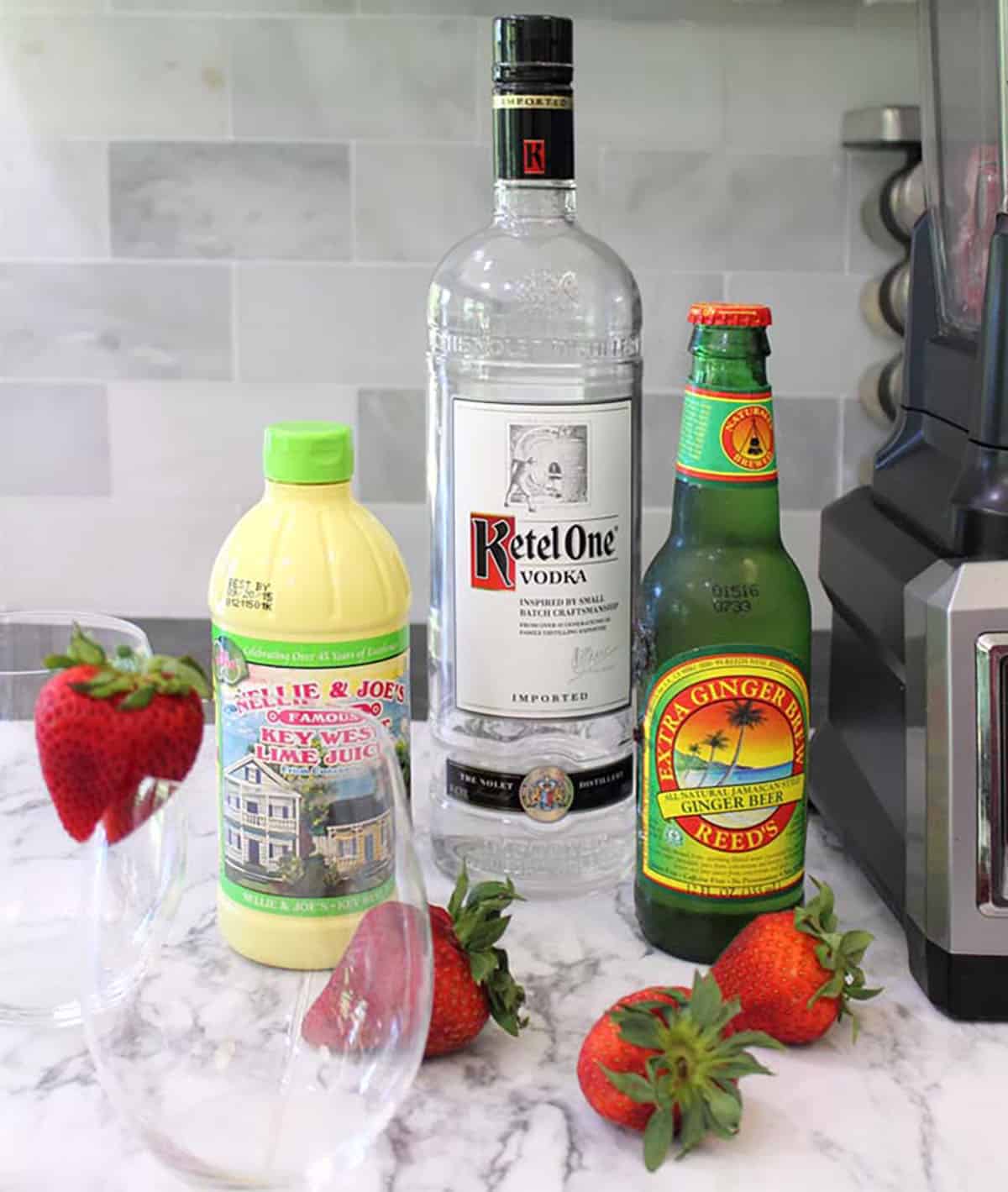 Moscow Mule ingredients - vodka, lime juice, strawberries, ginger beer on white table.