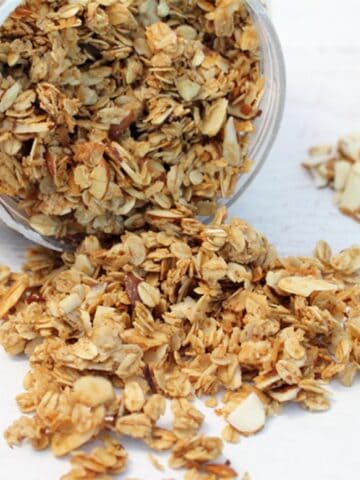 Granola spilling out of container showing crunchy oats, nuts and coconut.