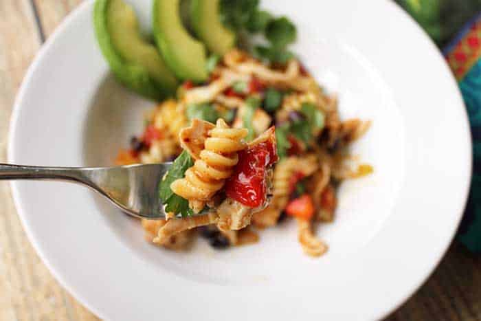 Bite of taco seasoned chicken and pasta above white bowl.