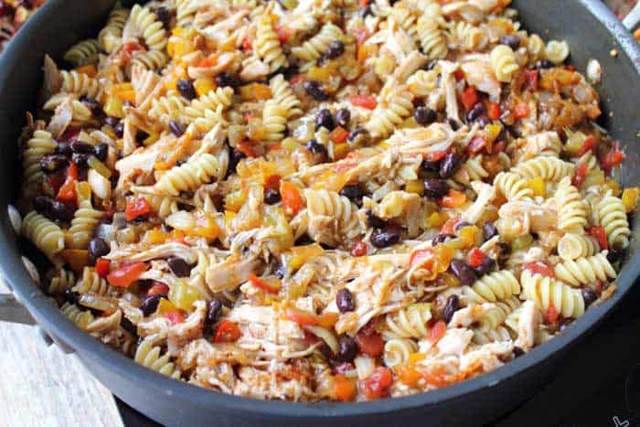 Simmered chicken, black beans, tomatoes and pasta in skillet.