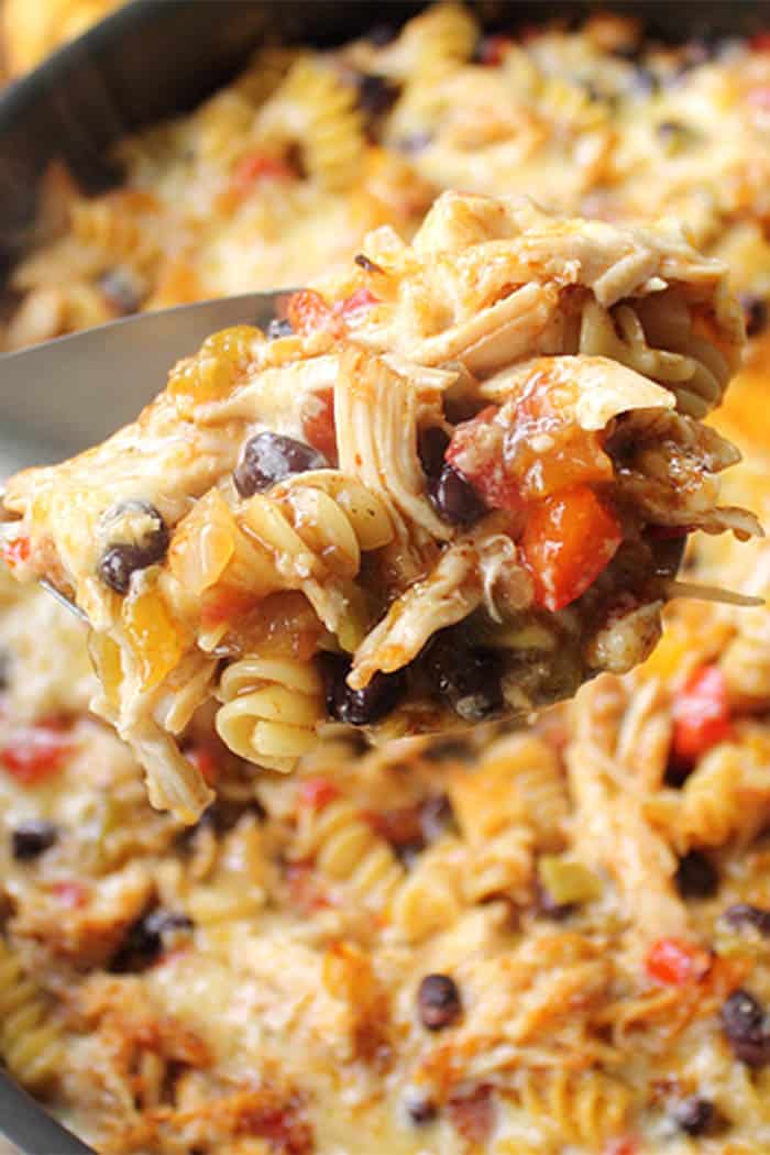 Closeup of spoonful of chicken, pasta, tomatoes and black beans above skillet.