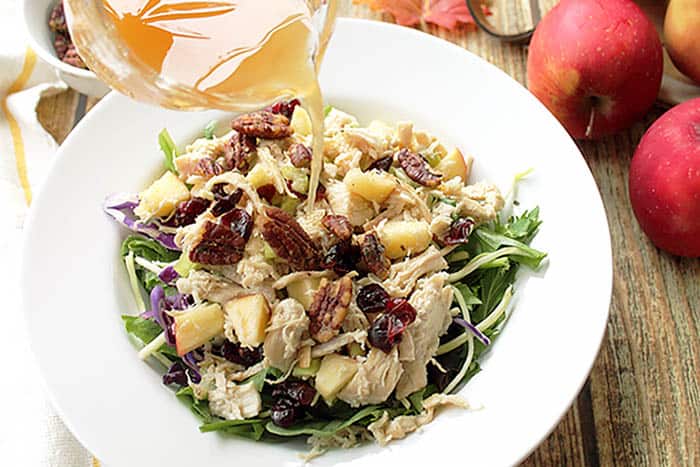 Pouring apple cider vinaigrette over apple chicken salad.