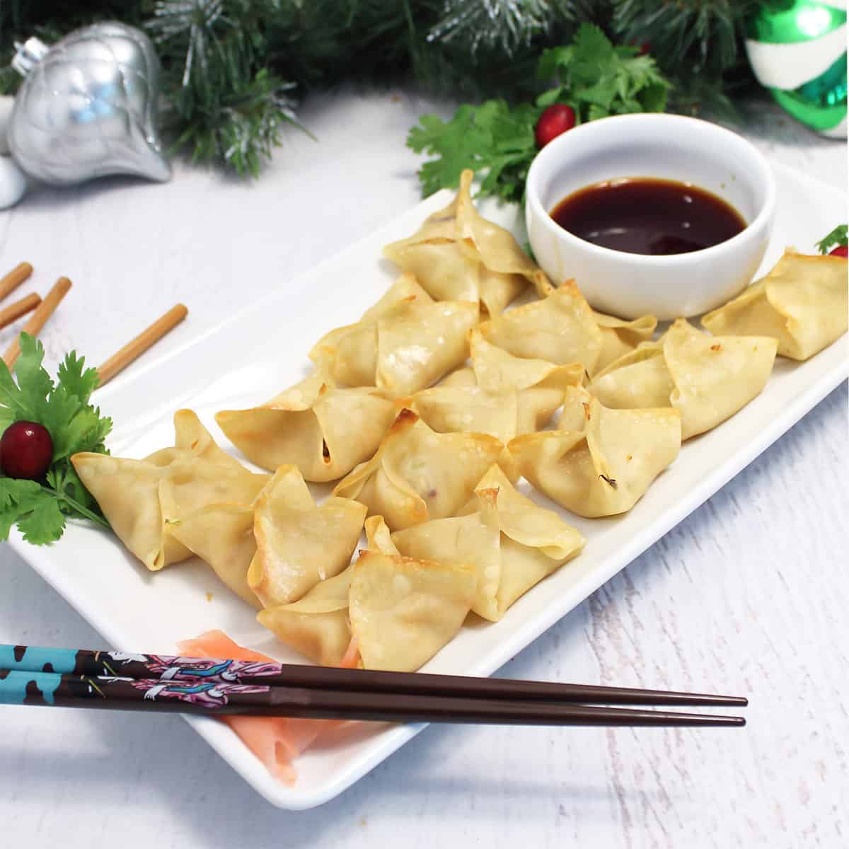 Baked wontons on white platter with Christmas deer and greenery in back.