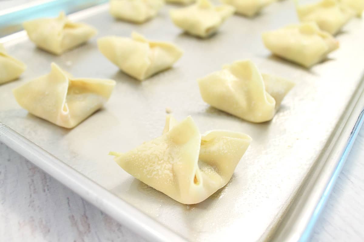 Filled chicken wontons on baking sheet ready for oven.