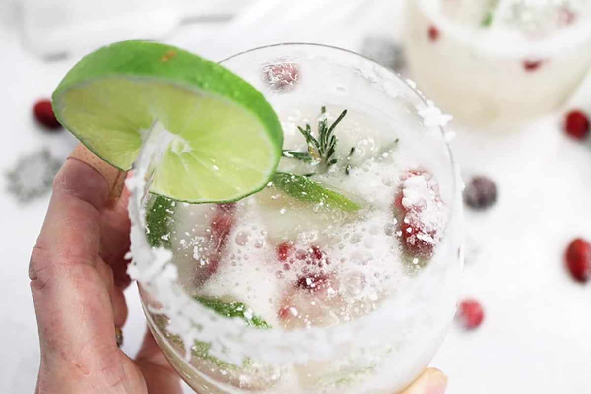 Closeup holding white christmas margarita to see coconut rim and holiday ice cubes.