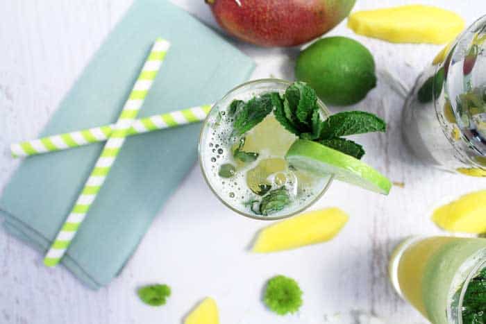 Overhead of cocktail with a mango, lime and 2 straws beside it.