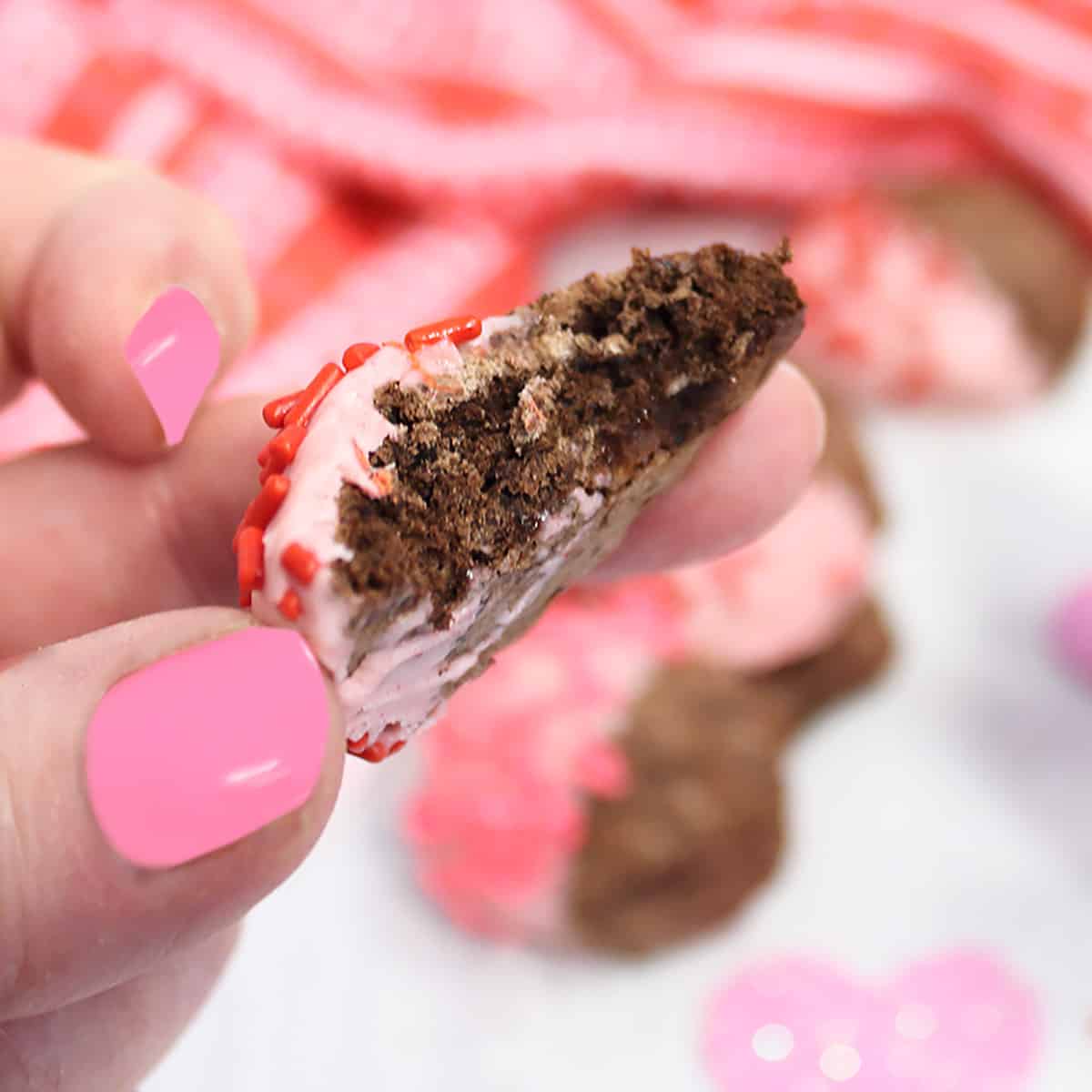 Holding chocolate meringue cookie with bite out of it.