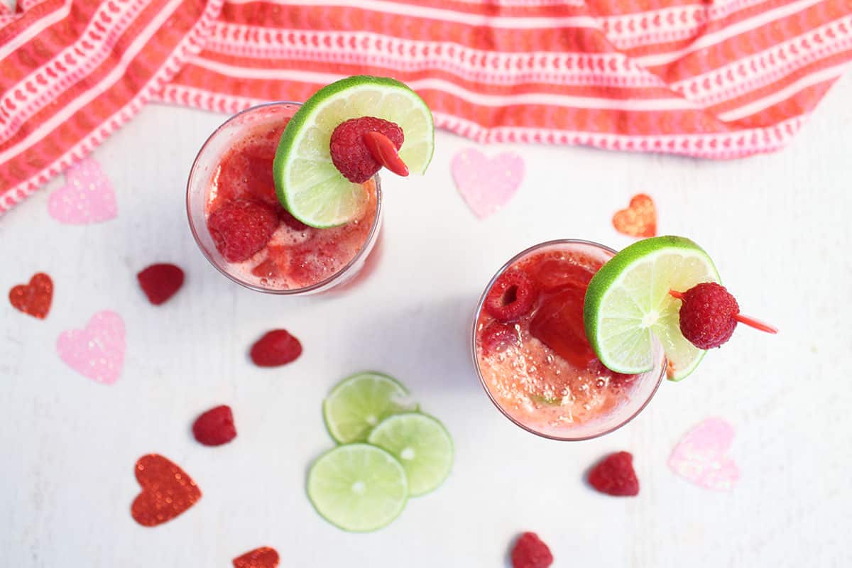 Overhead of two glasses filled with cocktail with Valentine towel in back.