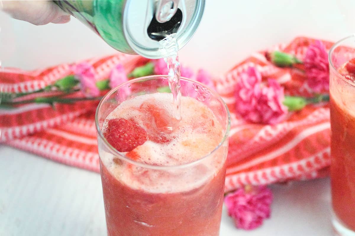 Pouring sparkling water into raspberry vodka drink.