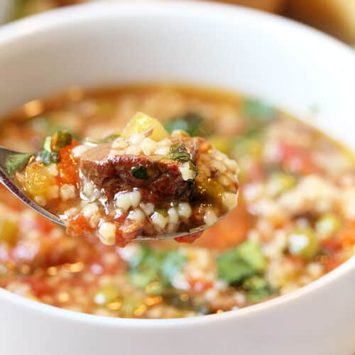 Spoonful of soup closeup over white bowl.