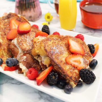 Strawberry stuffed French toast on platter topped with fruit.