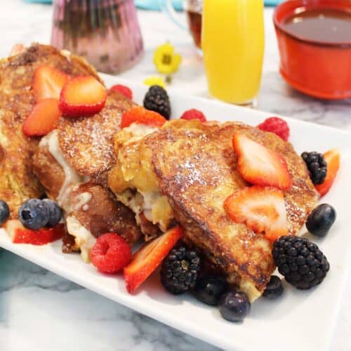 Strawberry stuffed French toast on platter topped with fruit.