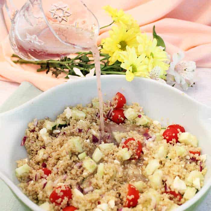 Greek Quinoa Salad pouring dressing square | 2 Cookin Mamas