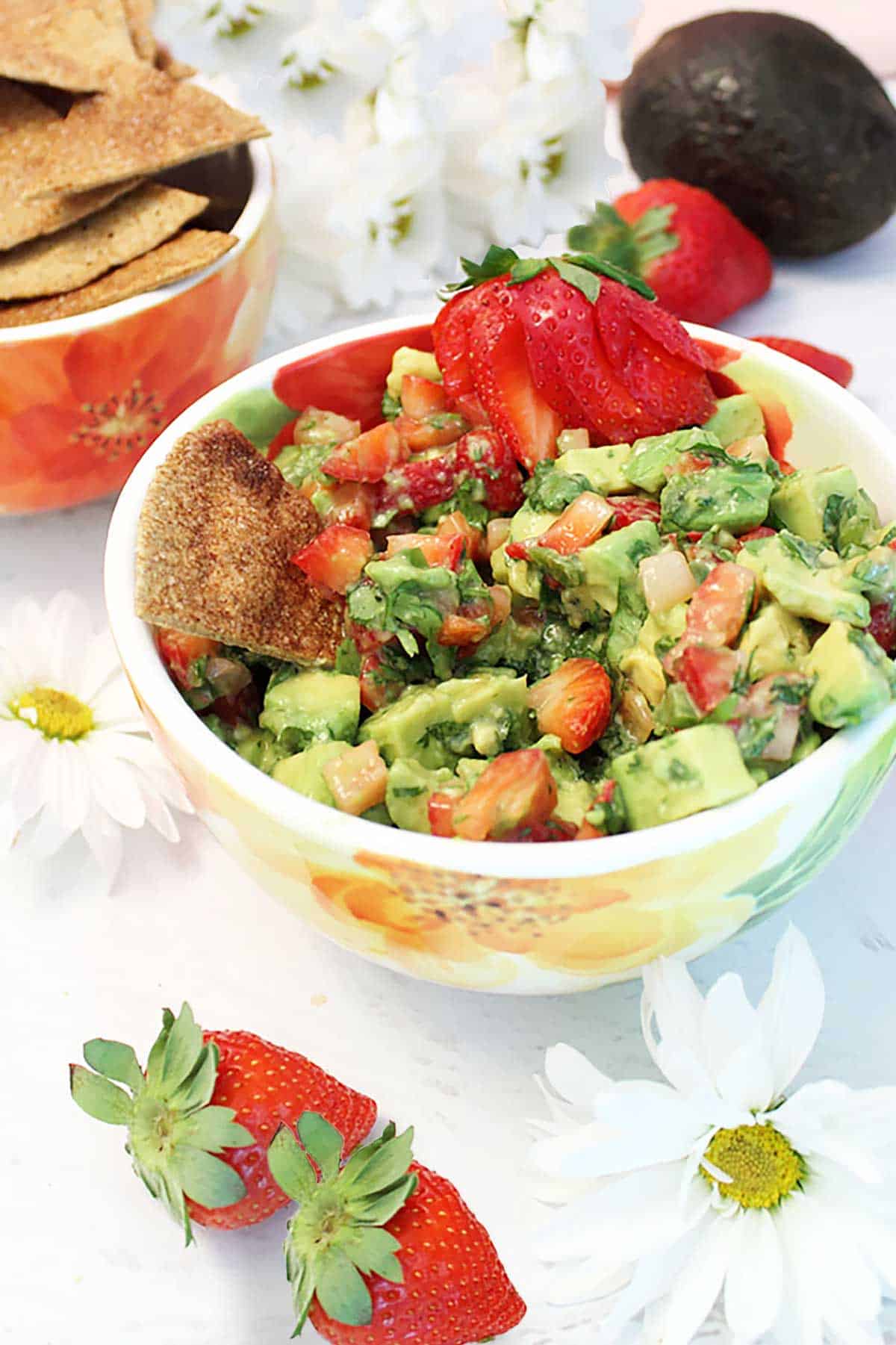 Strawberry Avocado Salsa on table with flowers and cinnamon chips.