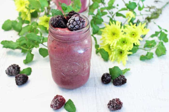 Blackberry Smoothie garnished with blackberries with flowers in background