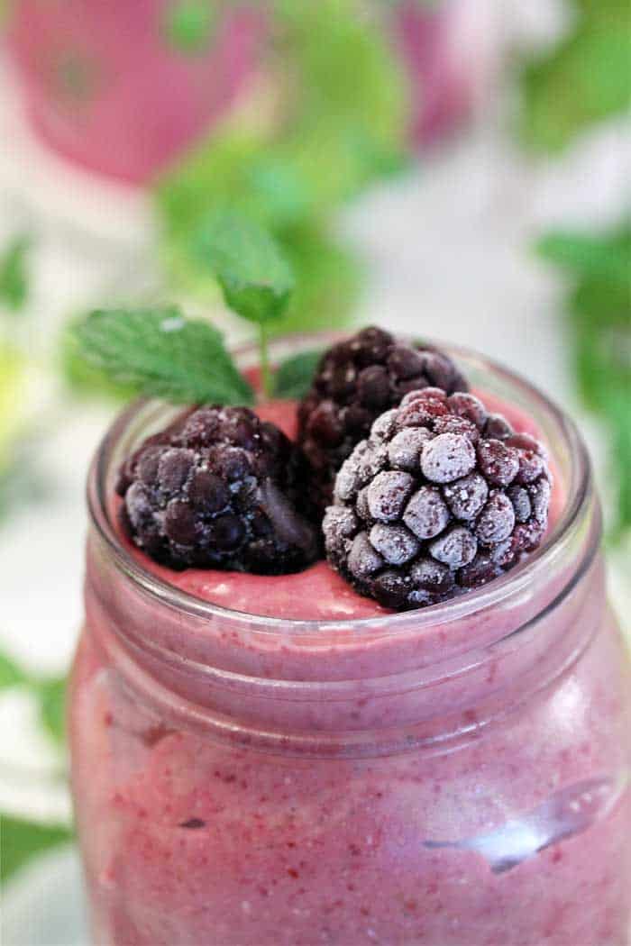 Closeup of frozen blackberries on top of smoothie in mason jar.