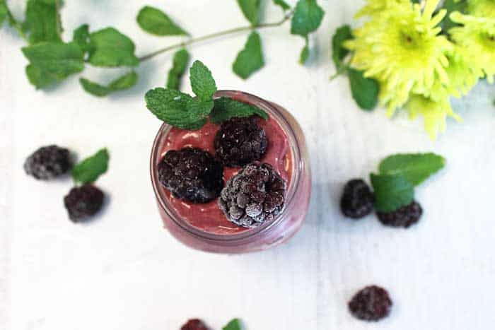 Overhead smoothie with a garnish of blackberries and mint on white table.