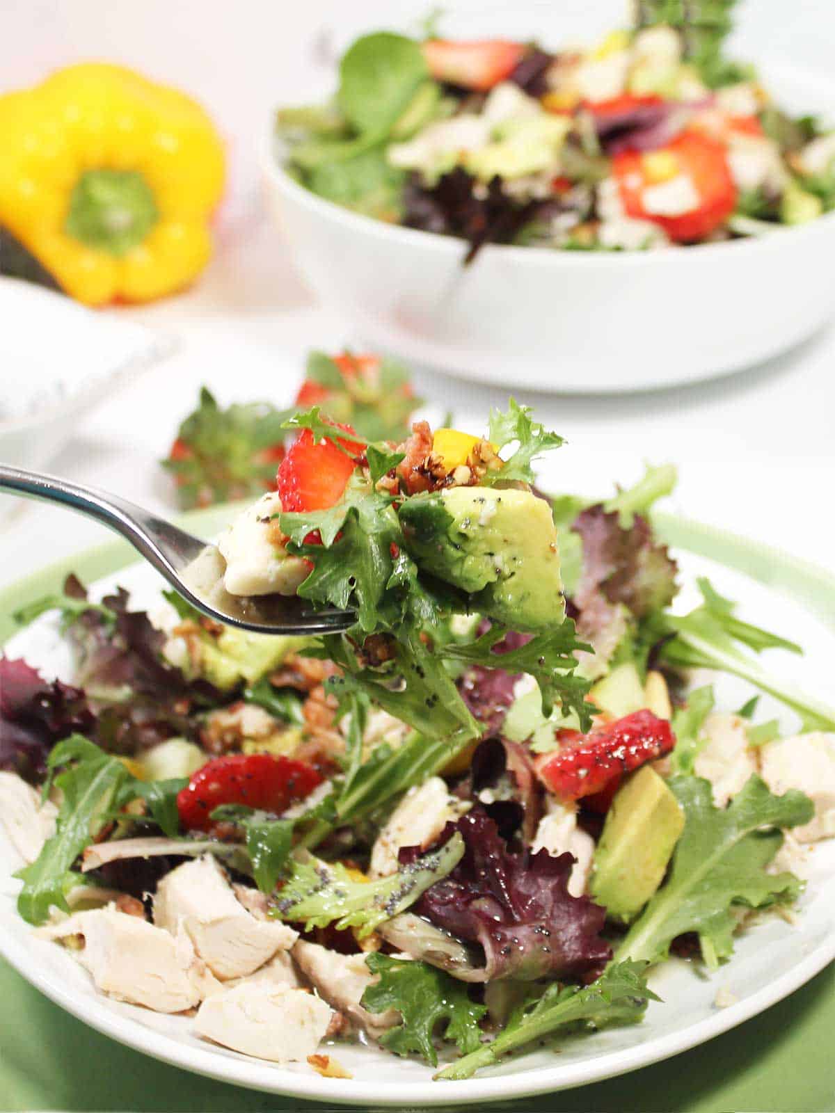 A bite of strawberry chicken salad on a fork over plate.