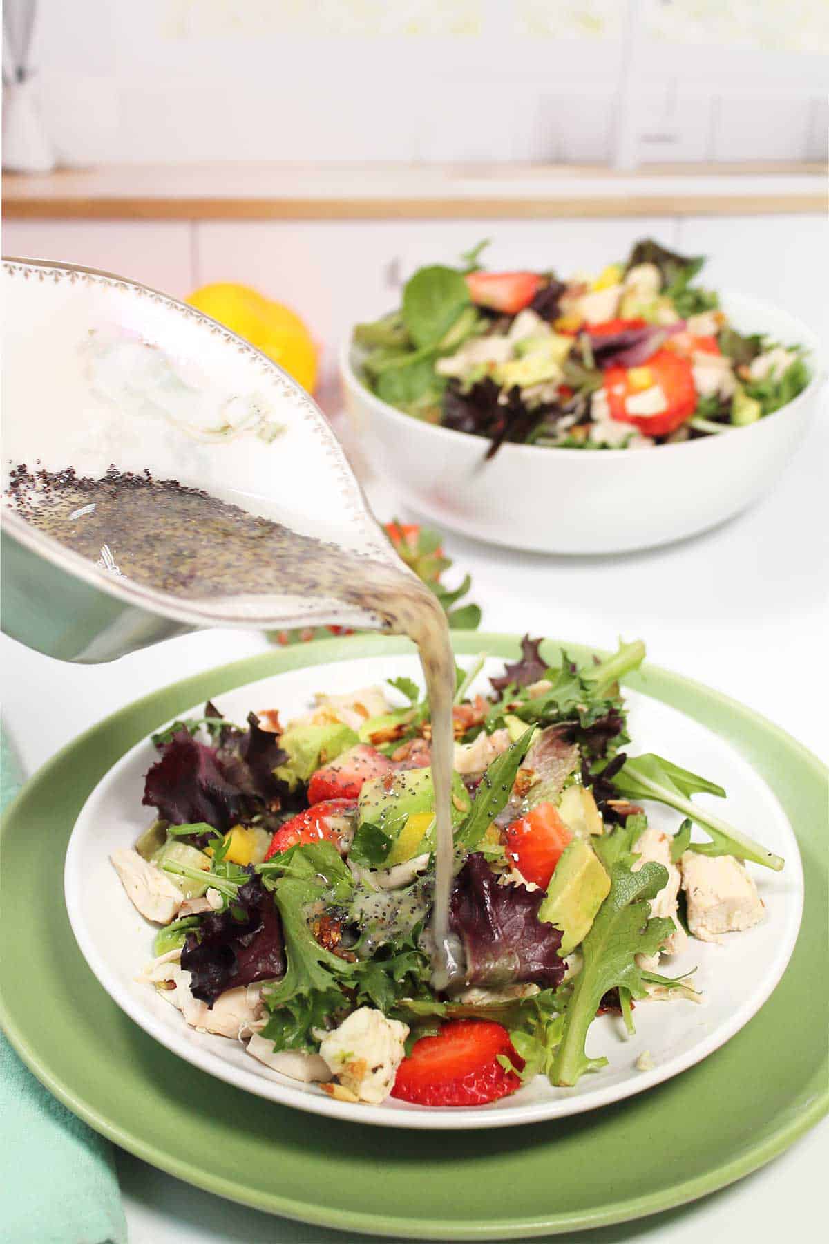 Pouring poppy seed dressing over plated salad.