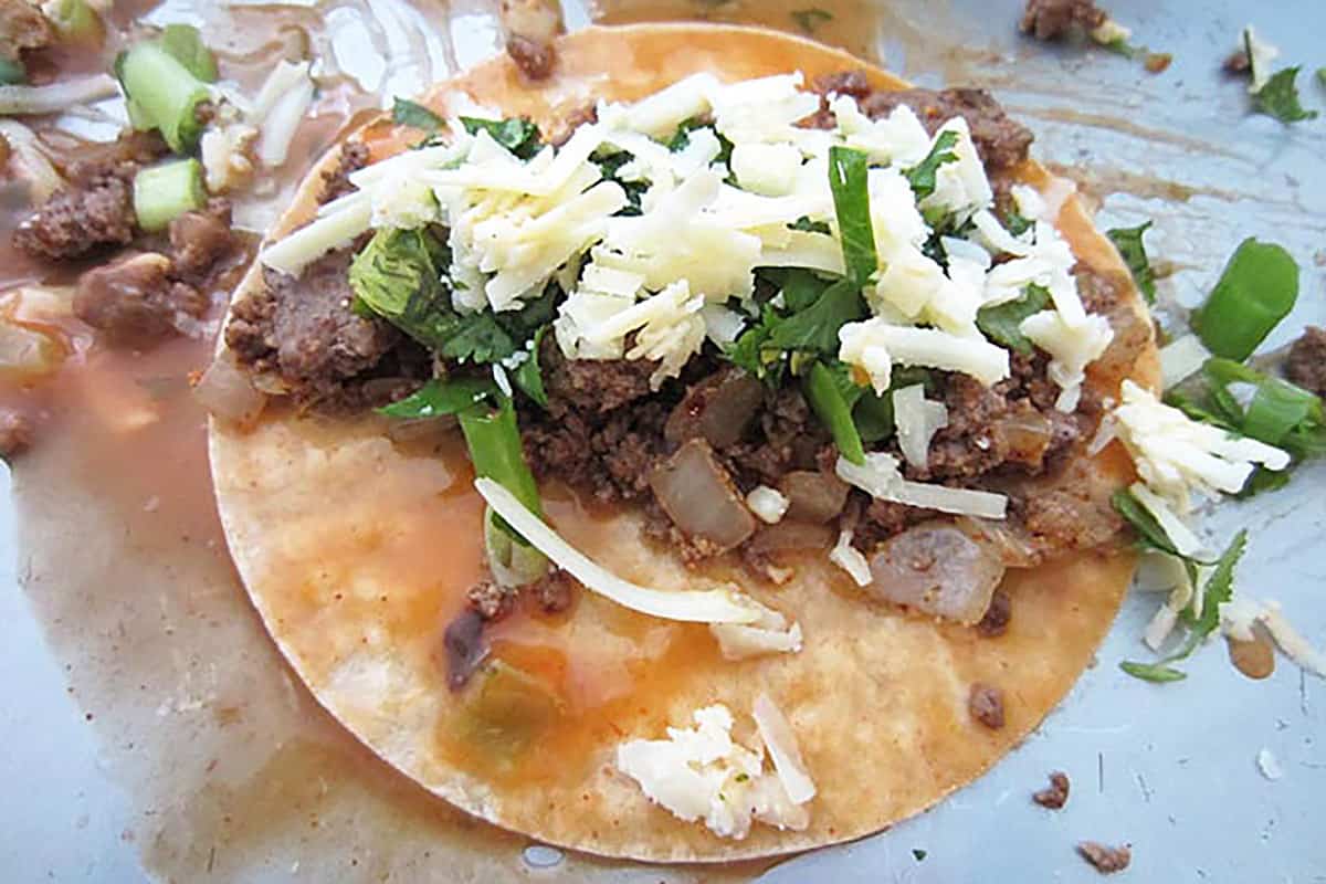 Topping corn tortilla with seasoned beef, cilantro and cheese before rolling.