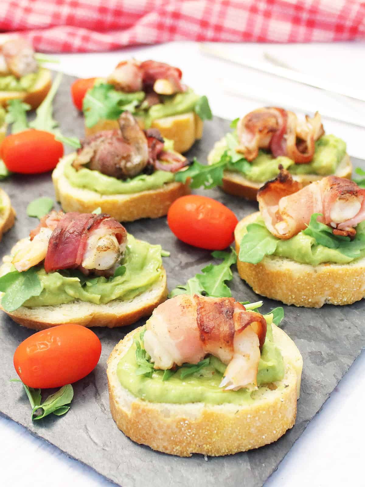 Bacon wrapped shrimp crostini on slate with arugula tomato garnish.