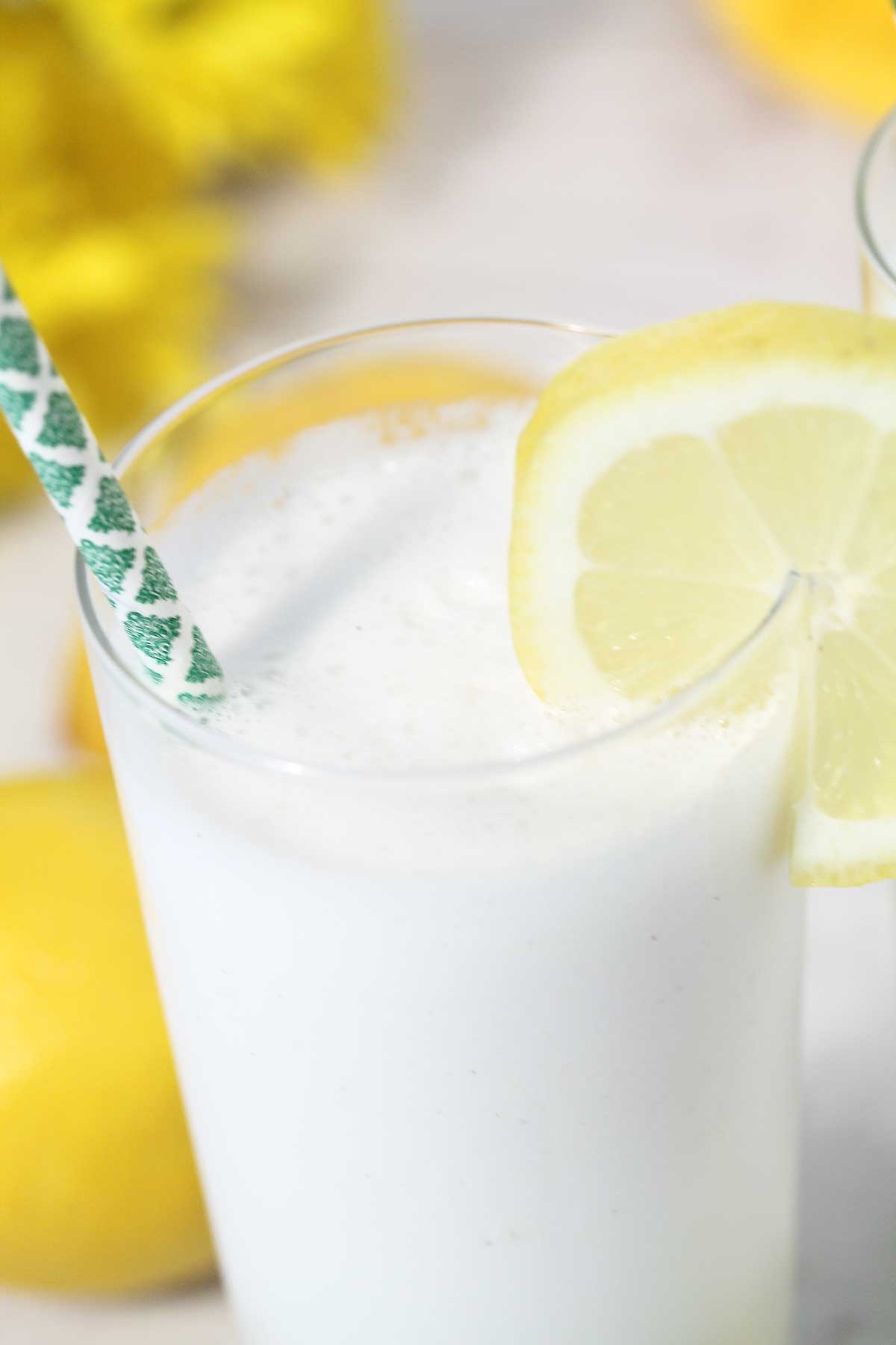 Closeup of frothy cocktail with straw and lemon garnish.