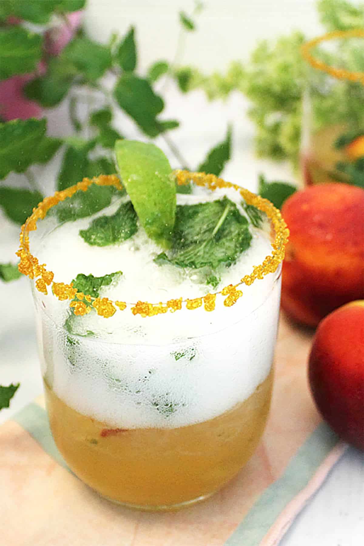 Mint Julep in glass with gold sugar rim with peaches beside it.