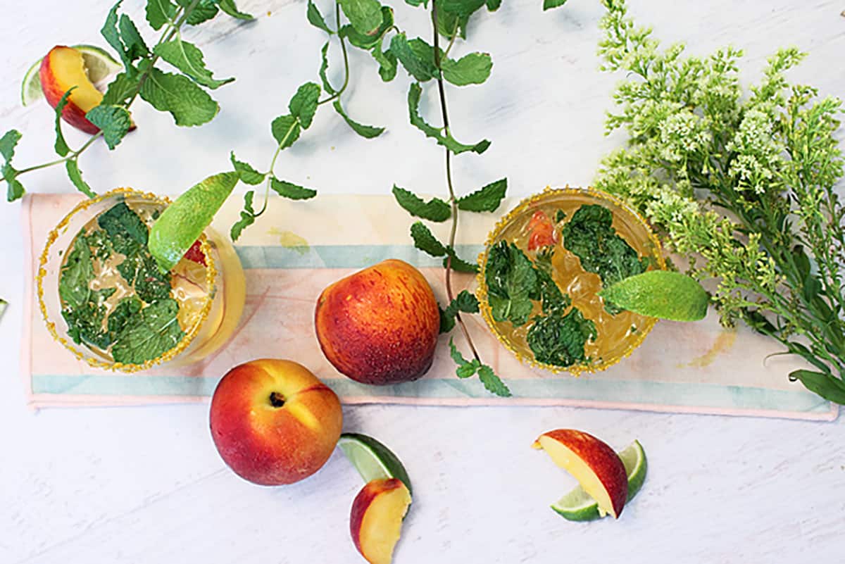 Overhead of 2 cocktails with peaches, mint and blossom sprig beside them.