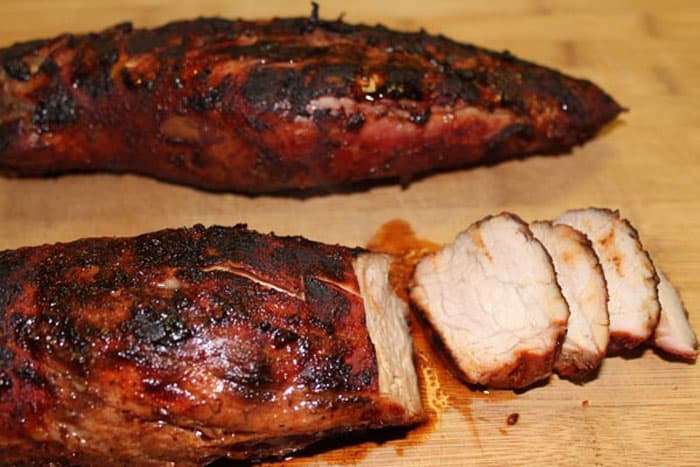 Sliced grilled pork tenderloin on wooden cutting board.