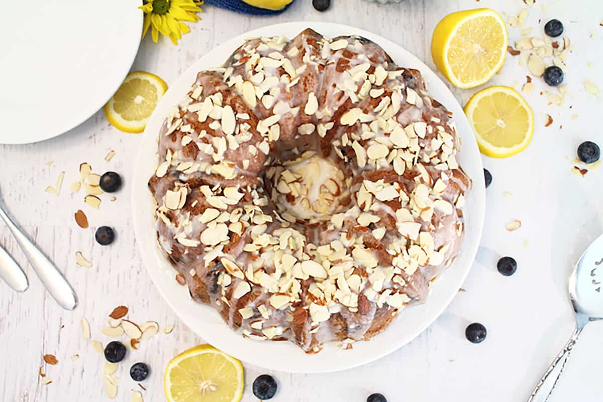 Overhead of almond cake with lemon icing with lemons and blueberries around it.