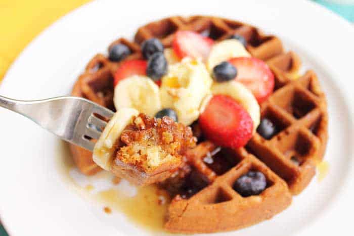 A closeup of a bite of banana waffle with slice on banana over the plate of waffles.