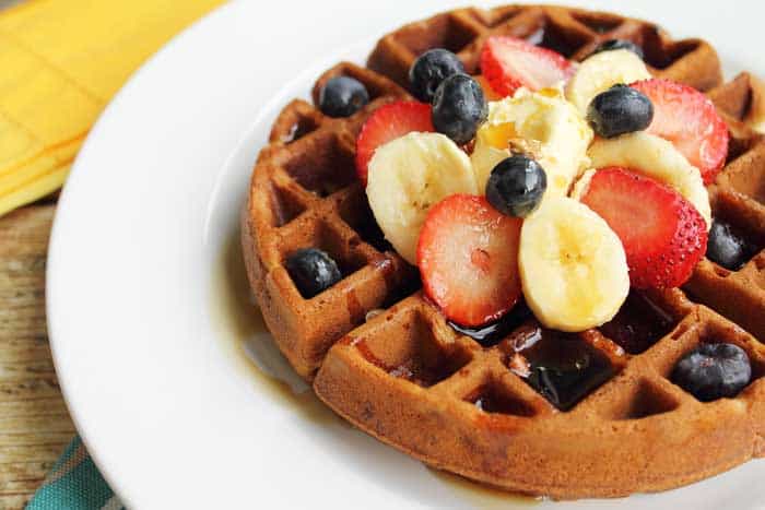 Closeup of full waffle showing crispy brown outside and garnishes of fruit.