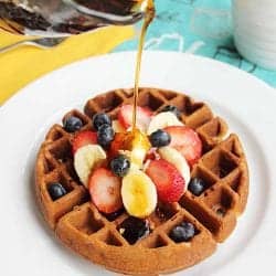 Pouring syrup over Banana Bread Waffles topped with sliced fruit.