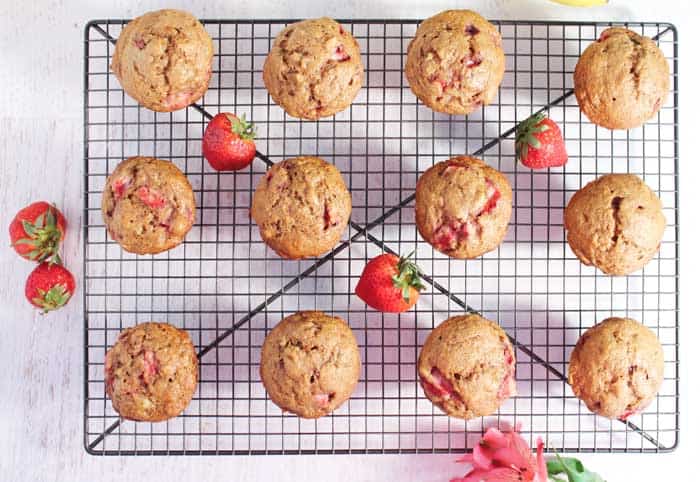 Baked muffins out of muffin tin, cooling on rack with strawberries scattered around.