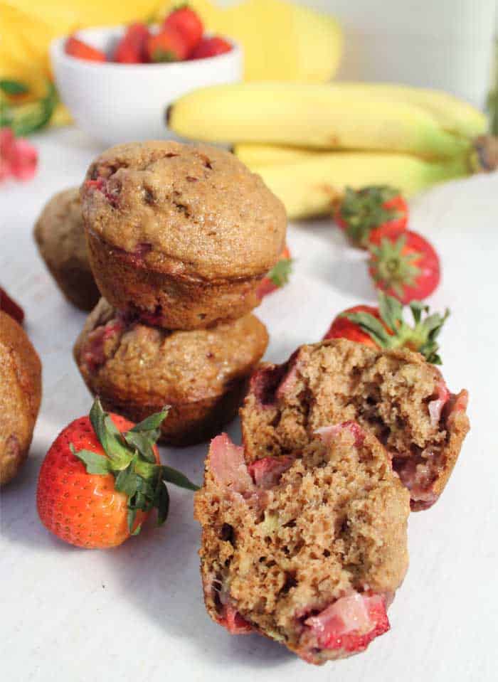 Stacked muffins on white table with one muffin cut open to show strawberries inside.