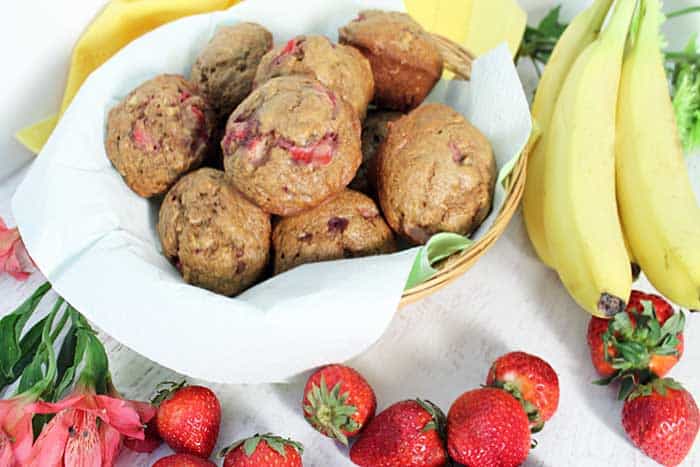 Overhead of Banana Strawberry Muffins in basket with bananas, strawberries and flowers beside it.