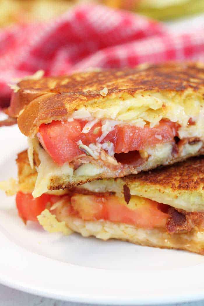 Closeup shot of inside of sandwich showing browned bread, oozing cheese and tomato.