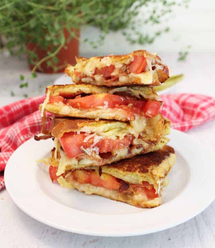 2 grille cheese cut in half and stacked on top of one another on white plate with red checkered towel in background.