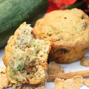 Bite of muffin on white table with zucchini in back.