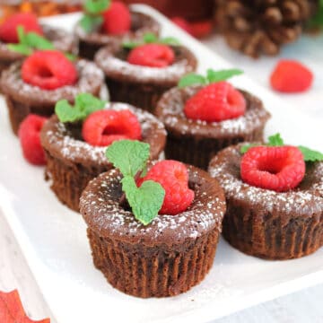 Molten chocolate cupcakes on platter with raspberry and mint garnish.
