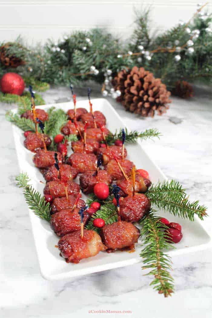 Bacon Wrapped Little Smokies on white plate with greenery and cranberry garnish.