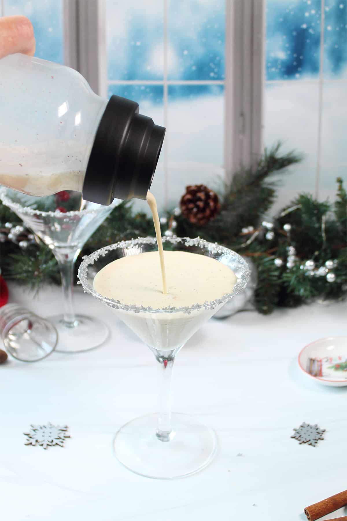 Pouring eggnog martini into silver sugar rimmed glass.