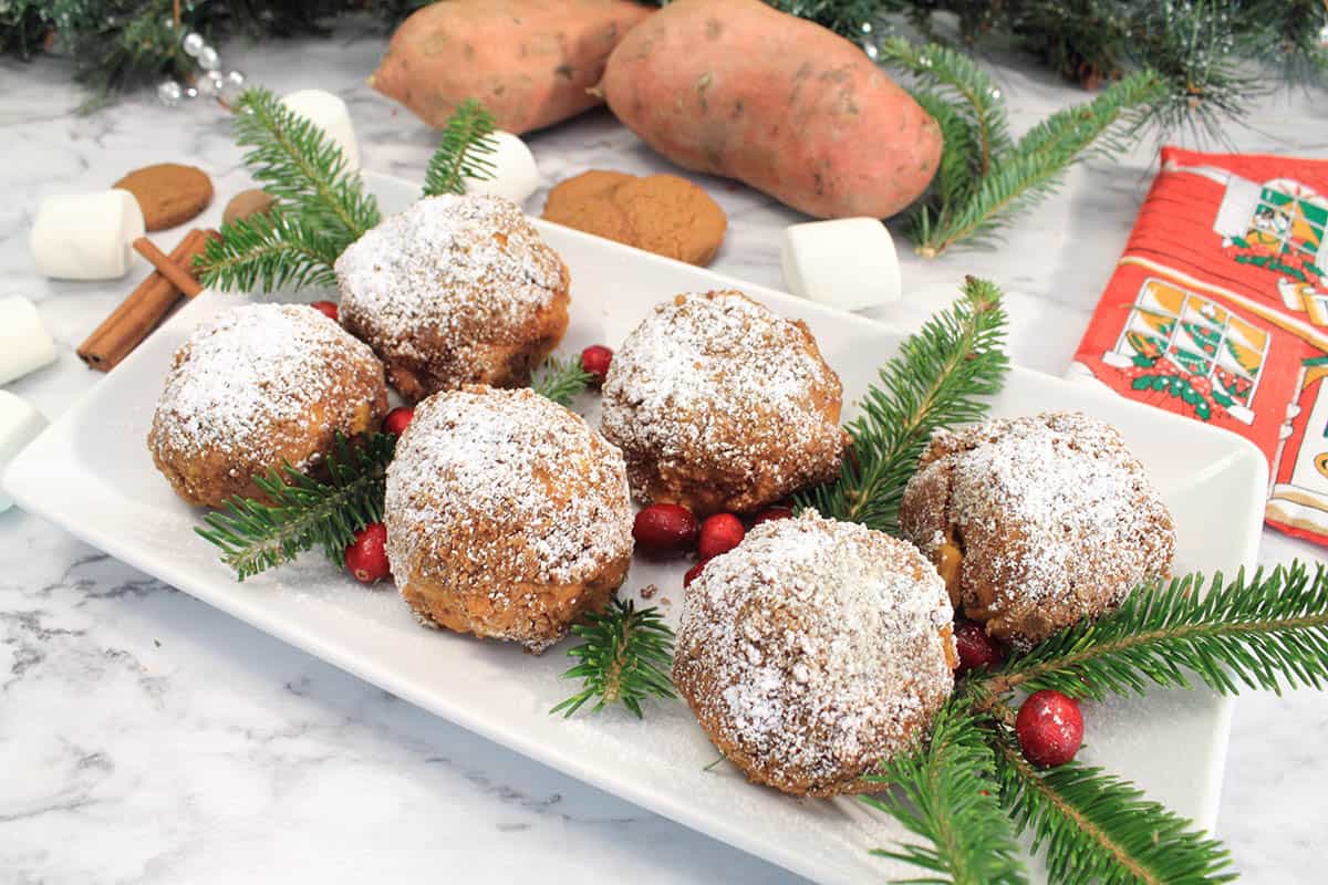 Plated sweet potato puffs with cranberries and pine garnish and sweet potatoes in back.